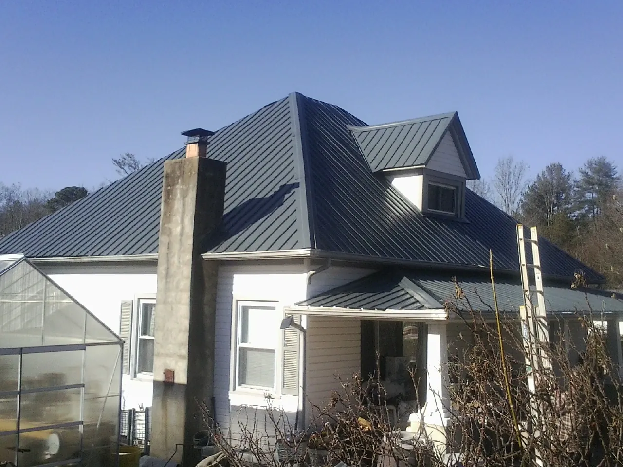 Dark blue standing seam metal roof on a white farmhouse with dormer — Slate & Tile Roof Repair by Roofing Brothers in Hunters