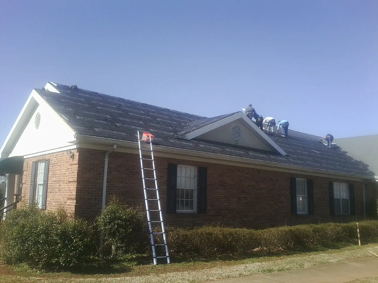 Crew tearing shingles off a brick ranch roof with a ladder set — Emergency Roof Repair work by our crew in Hunters