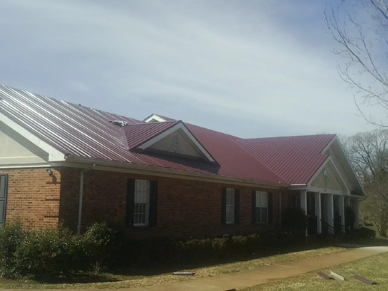 Red metal roof with gabled entries on a long brick building, from a Hail Damage Roof Repair job in Hunters