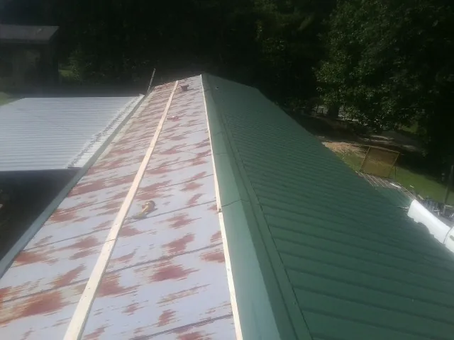 Old rusted panels beside newly installed green metal roofing — Wind Damage Roof Repair by Roofing Brothers in Hunters