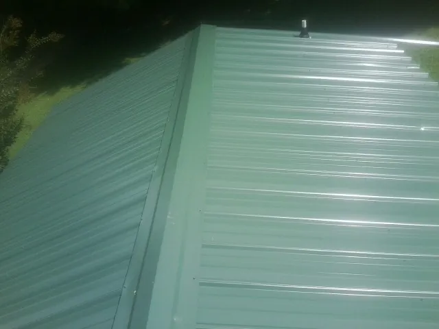 New green metal panels meeting at the ridge of a roof — Flat Roof Repair work by our crew in Hunters