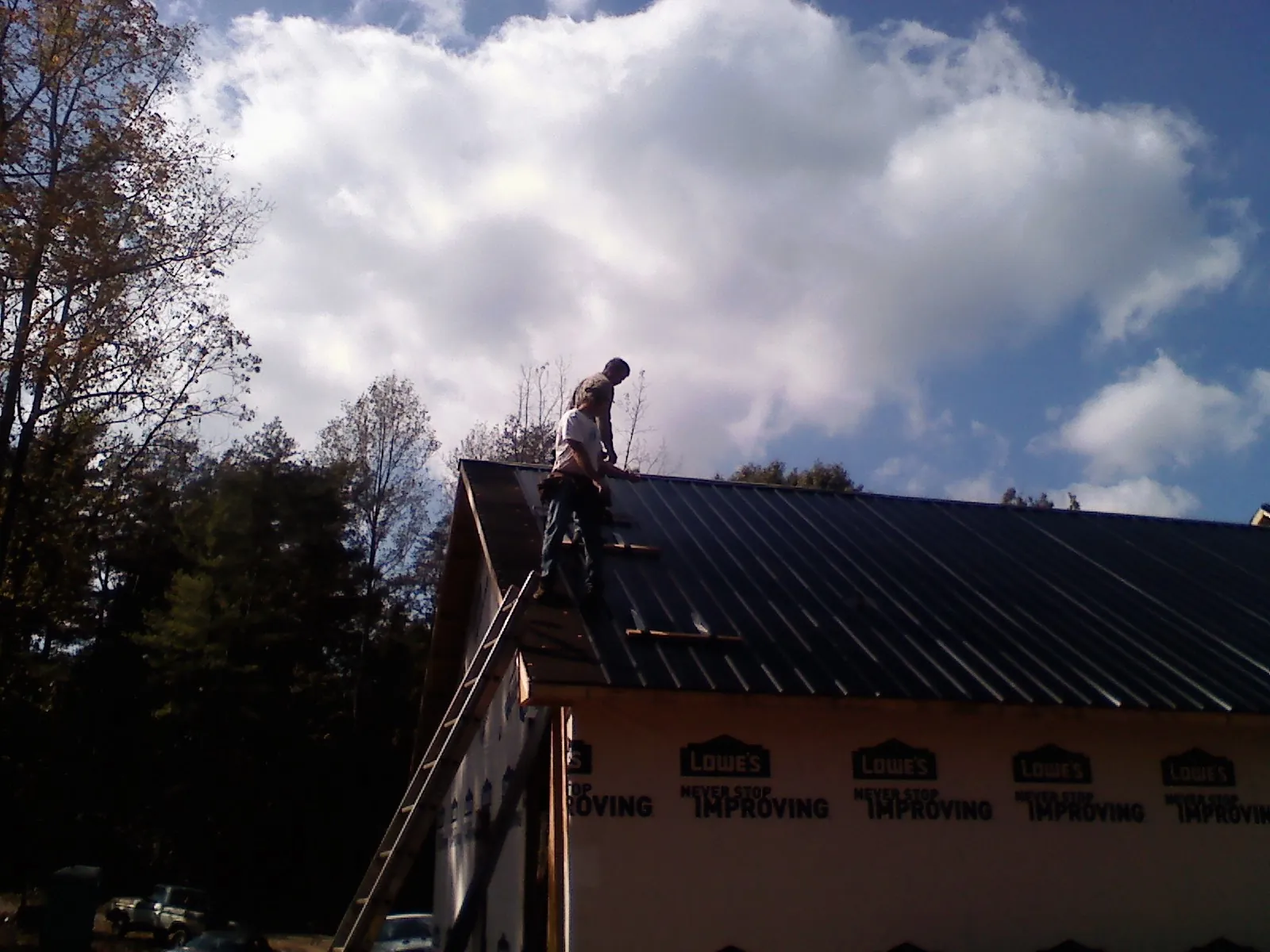 Roofer fastening dark metal panels high against a cloudy sky, from a Roof Inspection job in Hunters