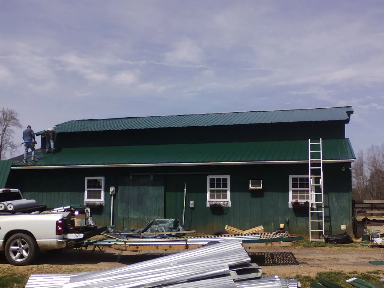 Crew installing green metal roofing on a large green barn in Hunters