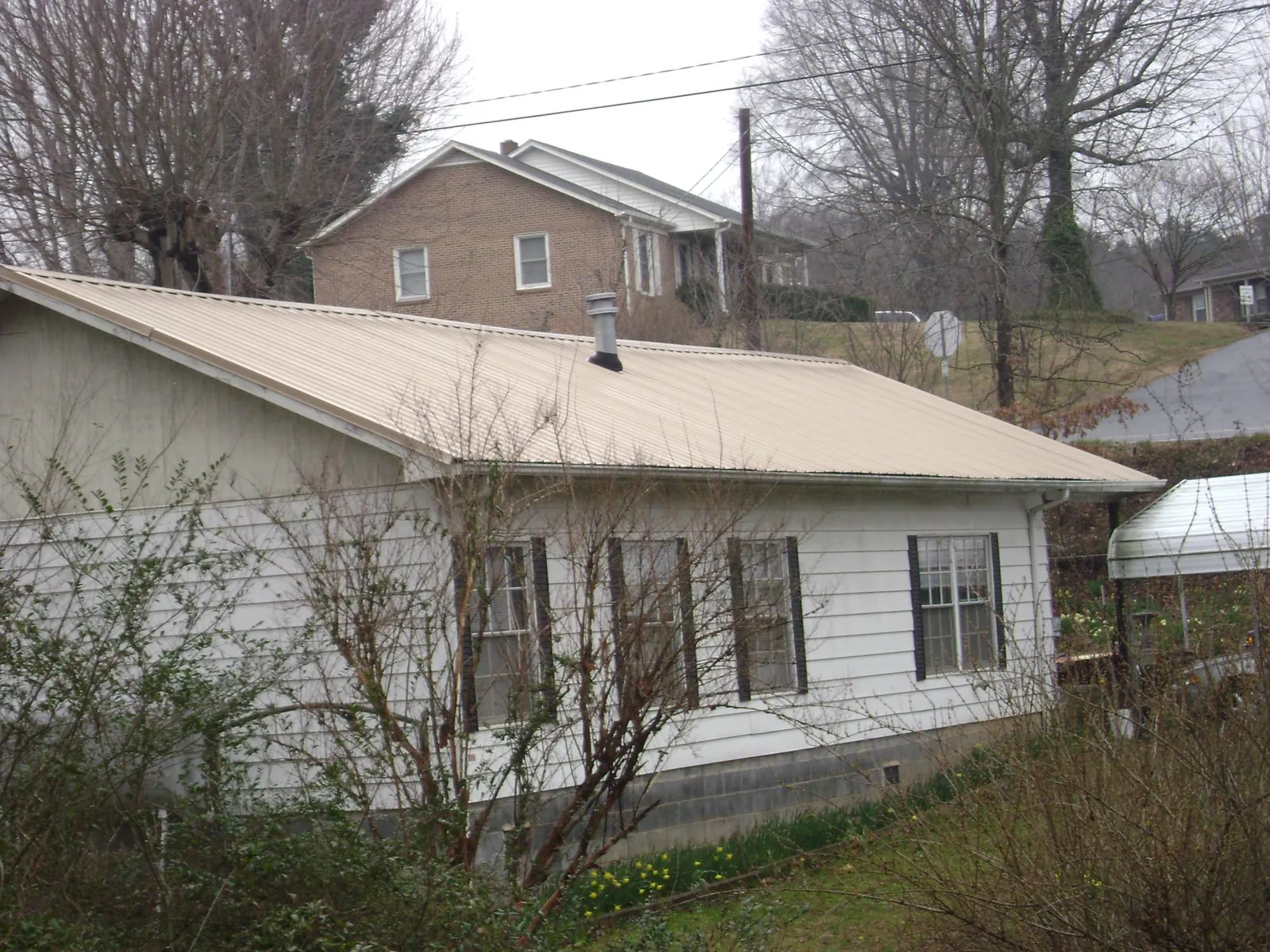 Tan metal roof on a white sided house set into a hillside — Commercial Roofing by Roofing Brothers in Hunters