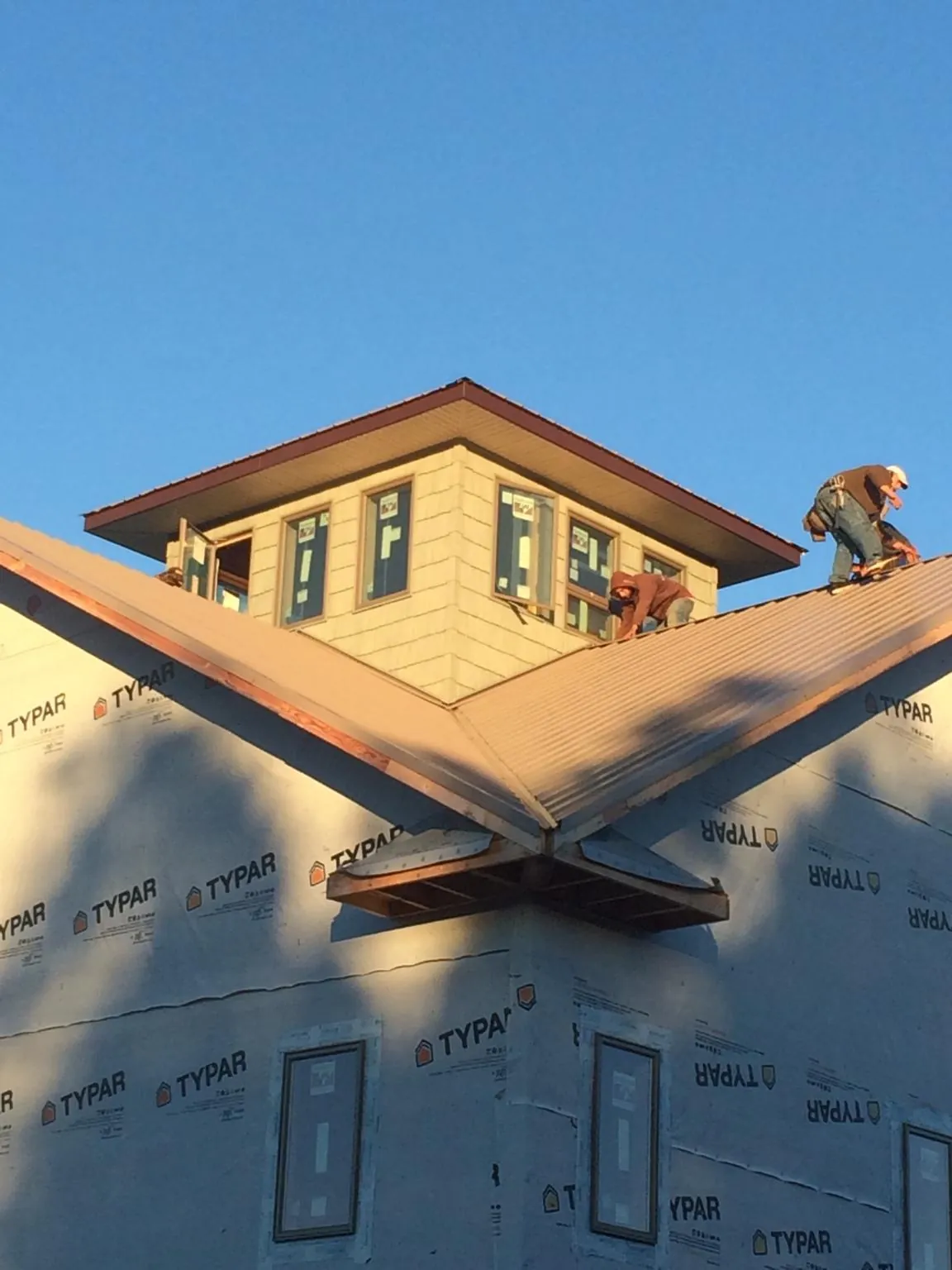 Roofers working around a rooftop cupola on a new metal roof at sunset — Roof Waterproofing in Hunters by Roofing Brothers